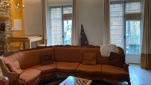 A living room with a sectional sofa, a wooden coffee table, a chandelier, and large windows with curtains.