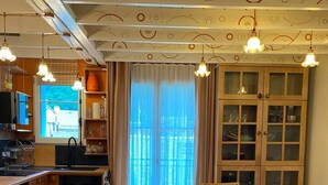 A kitchen with wooden cabinets, a dining table with chairs, and a window with curtains. - Jasmine, pretty hat, on a bicycle (Bagnères-de-Luchon)