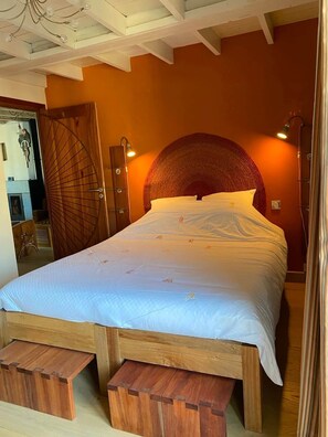 Une chambre à coucher avec un lit en bois, une grande tête de lit ronde et un banc en bois au pied du lit.