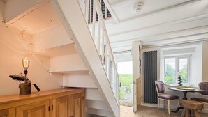 En trappe fører op til en balkon med et bord og stole, et træskab med en vintage lampe, og udsigt til grøn vegetation udenfor.