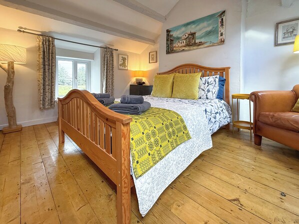 A bedroom with a wooden bed, a window with curtains, a painting on the wall, and a lamp.
