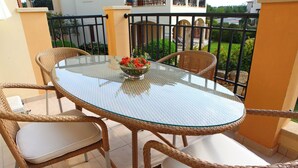 A glass-top table with wicker chairs and a white cushion, surrounded by a black metal railing. - 1 Bedroom Apartment - BC11 (kouklia)