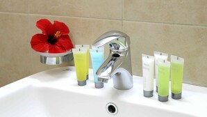 En handfat i badrummet med en kromad blandare, en röd hibiskusblomma och fyra tuber lotion med etiketten ”ger en känsla av fräschör”.