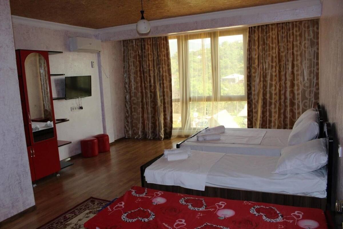 A bedroom with two beds, a TV, a mirror, and a window with curtains.