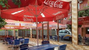 Outdoor seating with red umbrellas, tables, and chairs, some labeled "Bavaria". - Llia hotel  (Kobuleti)