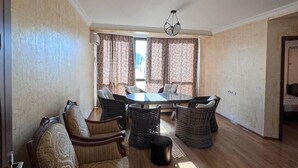 A spacious living room with a large round table, multiple wicker chairs, a sofa, and a view through large windows with curtains. - Llia hotel  (Kobuleti)