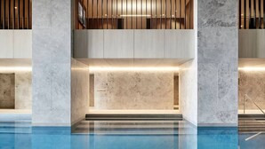 Area piscina interna moderna con vista chiara sull'acqua, parete in marmo e soffitto in listelli di legno.