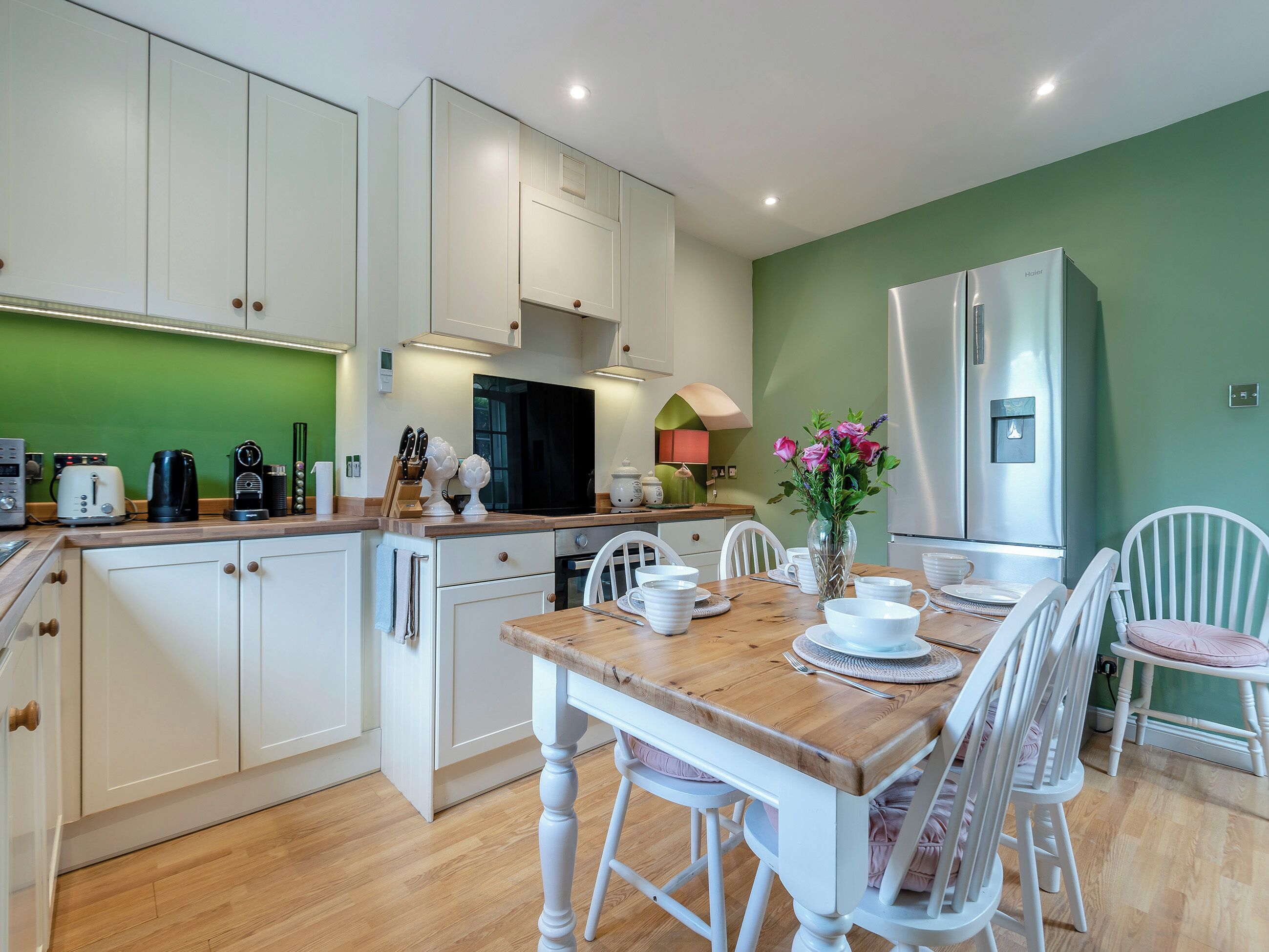 Una cocina moderna con armarios blancos, una mesa de comedor de madera y un refrigerador.