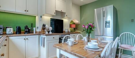 Una cocina moderna con armarios blancos, una mesa de comedor de madera y un refrigerador.
