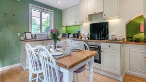 Cocina con armarios blancos, una mesa de madera y sillas. Se ve vegetación a través de la ventana.