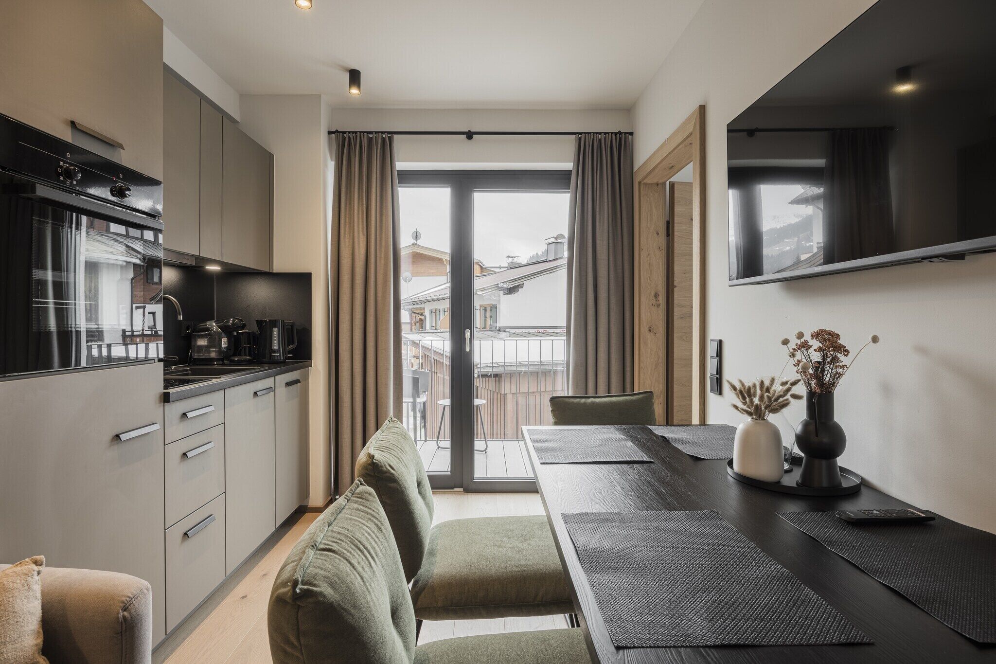 Une cuisine moderne dotée d’une cuisinière intégrée, d’un coin repas avec une table et des chaises, et d’une grande fenêtre agrémentée de rideaux.