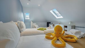 Une chambre d’hôtel moderne avec deux lits, une lucarne, un grand jouet en peluche en forme de poulpe et un lit soigneusement fait avec des serviettes.