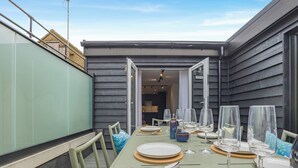 Un espace de restauration en plein air avec une table dressée pour six personnes, comprenant des verres à vin et des couverts.