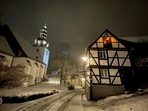 A snow-covered street with traditional buildings, including a half-timbered house and a church with a clock tower. - Small community center at the bell tower in the middle of the historic old town (Arnsberg)