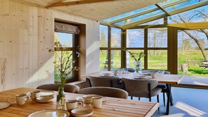 Een eetruimte met houten tafels en stoelen, grote ramen en uitzicht op het landschap.