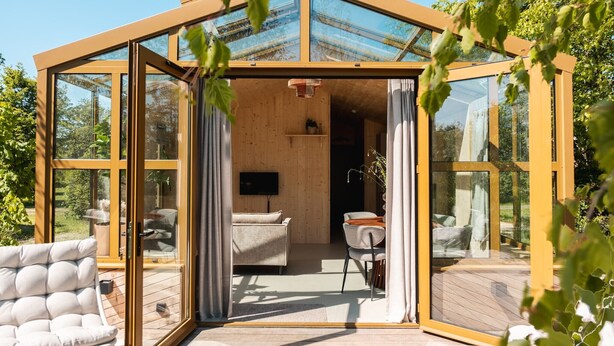 Een kamer met glazen wanden, een houten plafond, een bank, een tafel en een televisie.