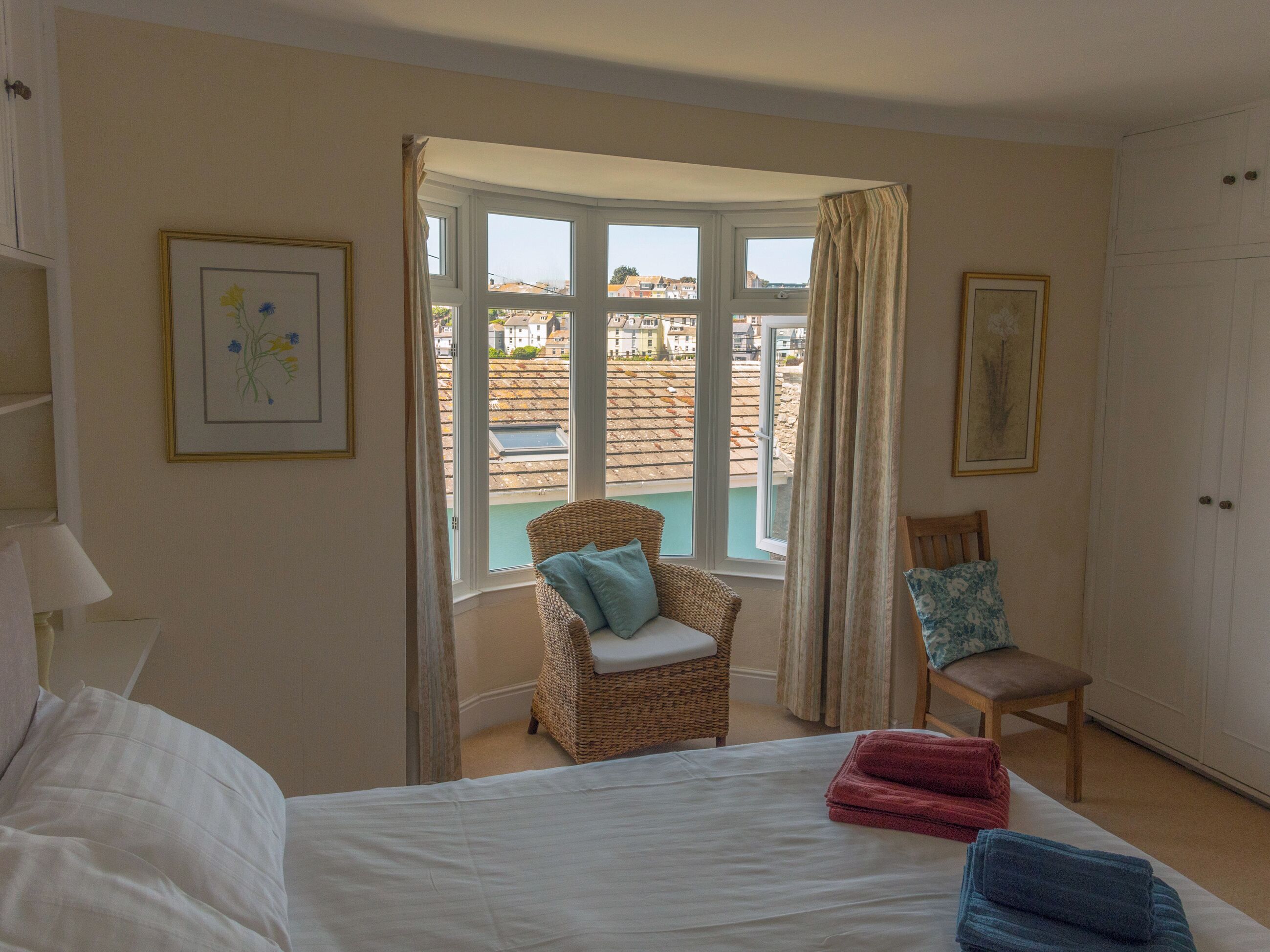 Ein Schlafzimmer mit Bett, Stuhl, Kleiderschrank und Fenster mit Blick auf Gebäude.