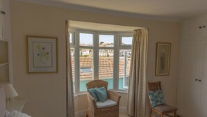 A bedroom with a bed, a chair, a wardrobe, and a window with a view of buildings. - 2 bedroom accommodation in Brixham (Brixham)