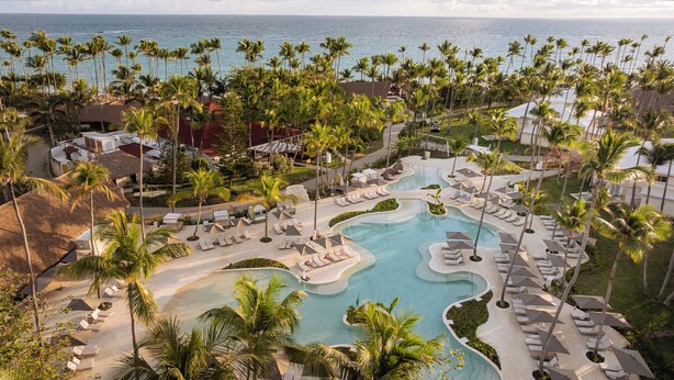 A resort with a pool, palm trees, and a view of the ocean.