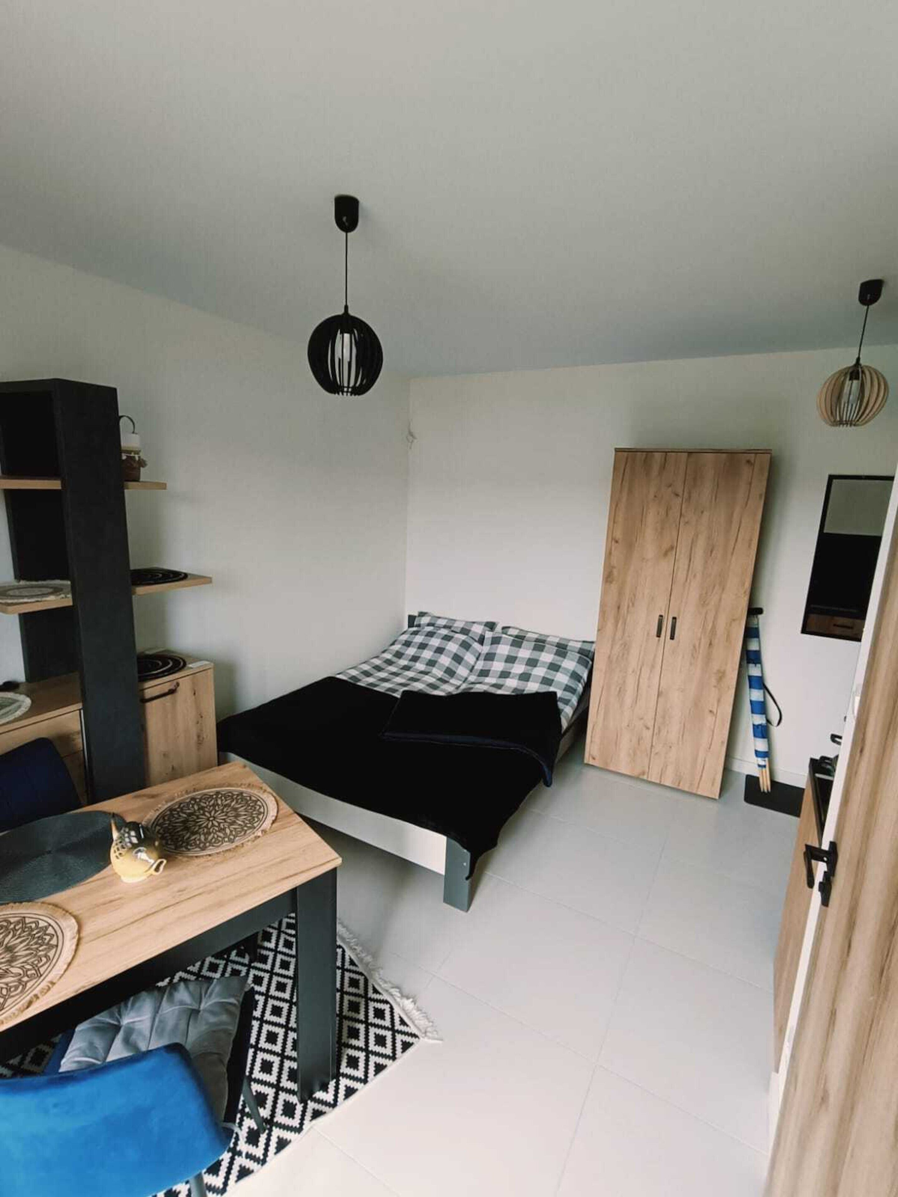 A compact room with a bed, a desk, a wardrobe, and a hanging light fixture.