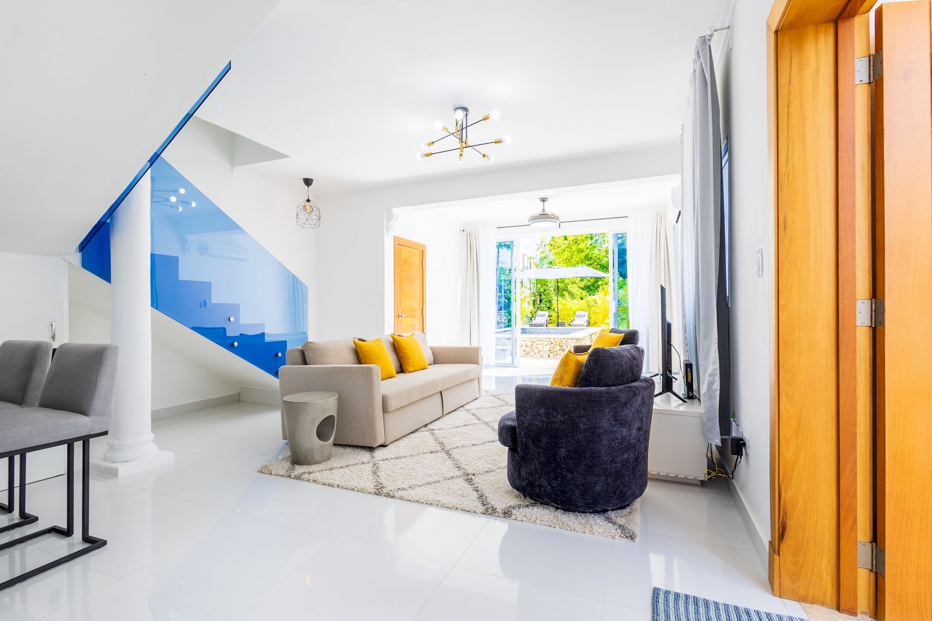 A modern living room with a staircase, a sofa set, and a view of the outdoors.
