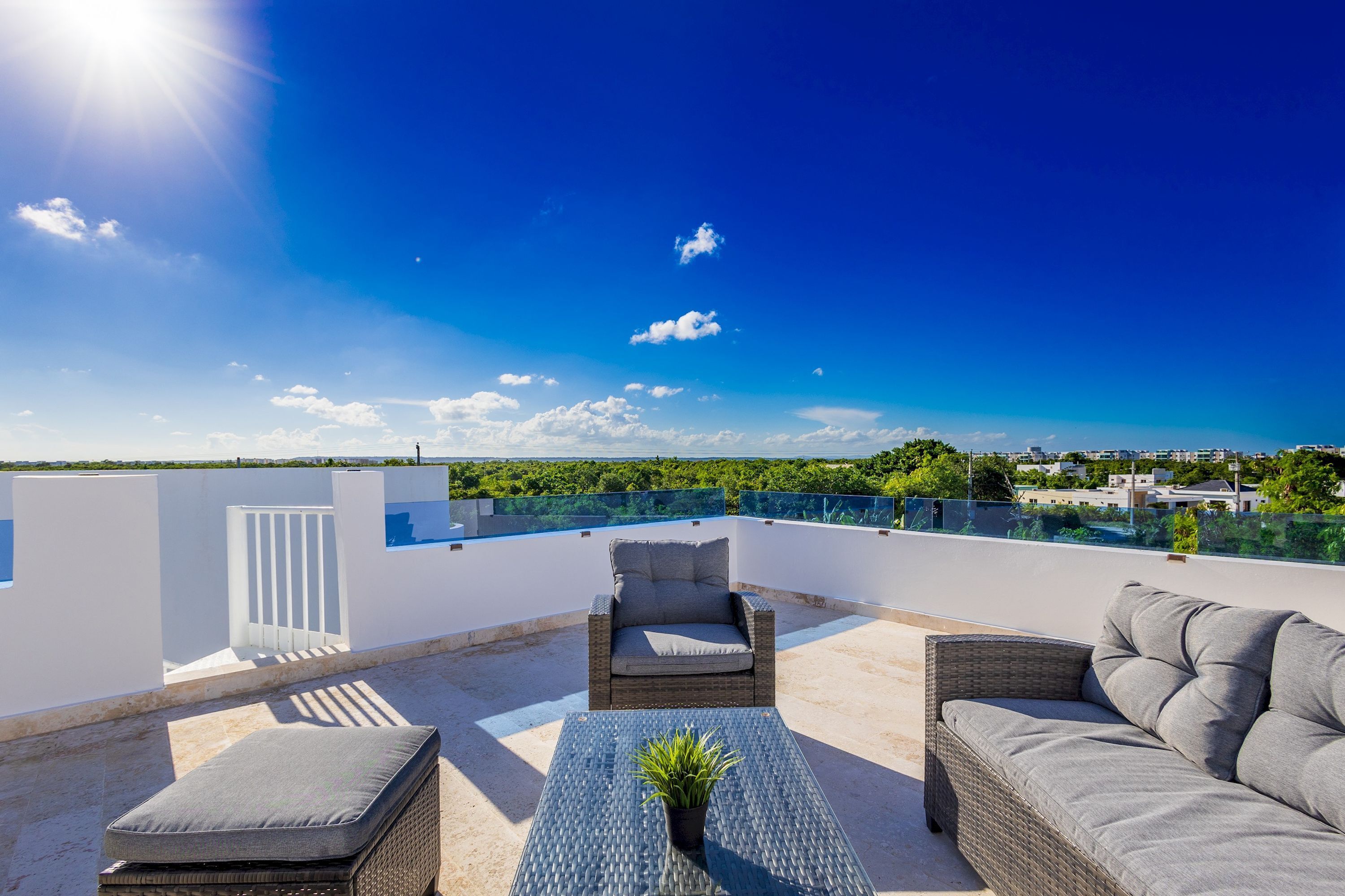 A rooftop terrace with a wicker sofa, a cushioned chair, and a small table with a plant.