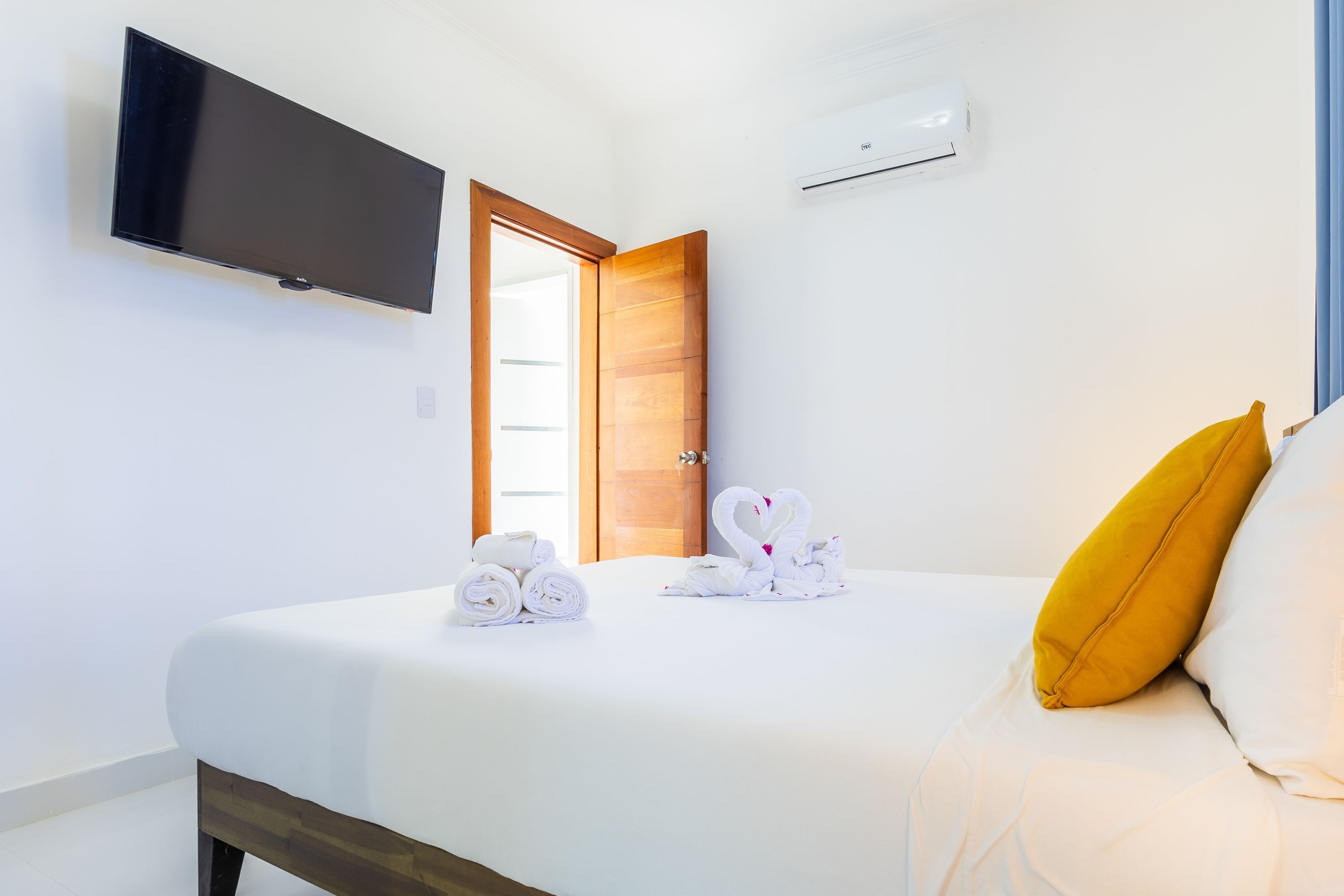 Una habitación de hotel con una cama, un televisor de pantalla plana montado en la pared, un equipo de aire acondicionado y una puerta de madera.