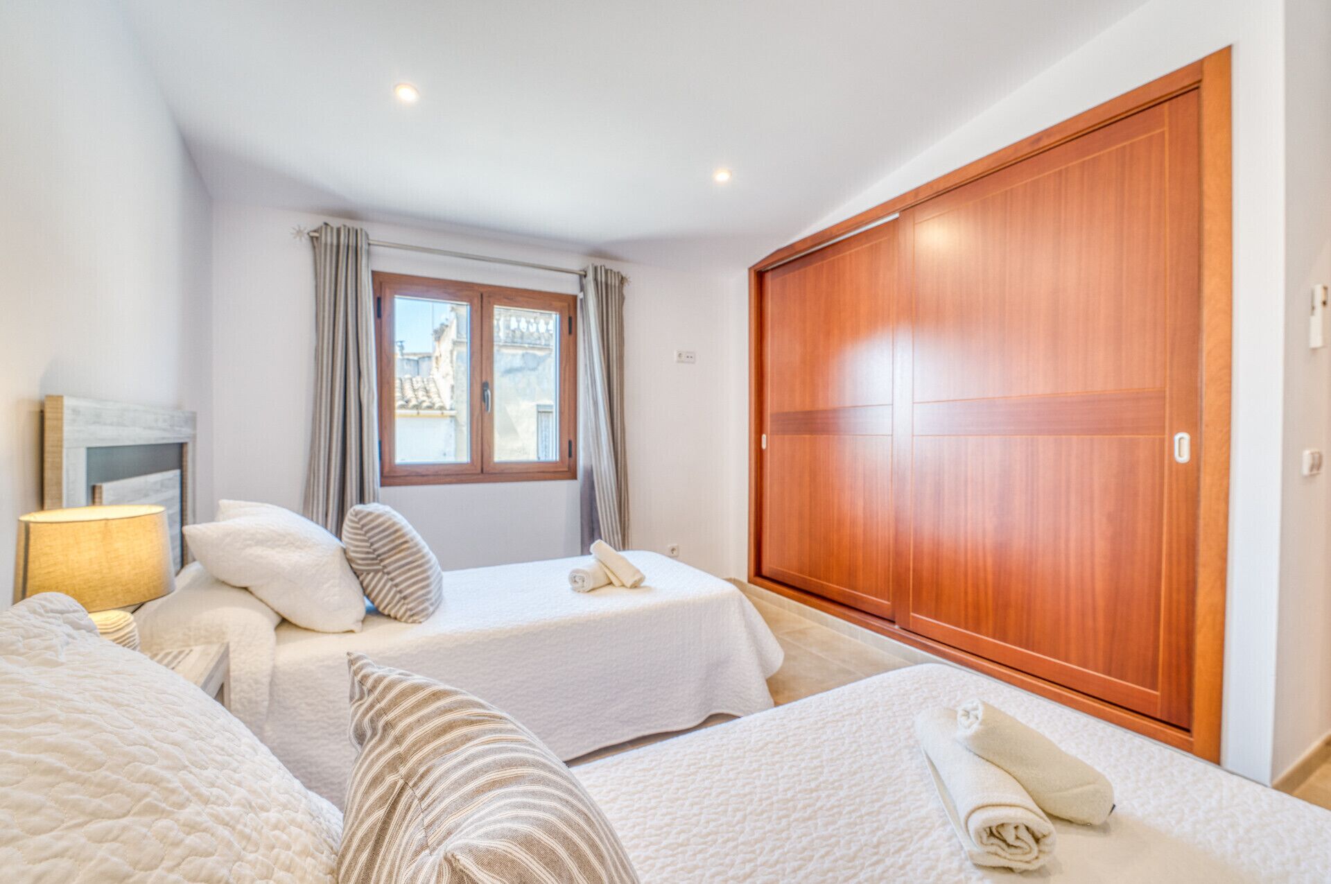 Une chambre avec deux lits, une armoire en bois, une fenêtre avec des rideaux et une lampe de chevet.