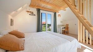 A bedroom with a large bed, a wooden staircase, and a desk with a chair.