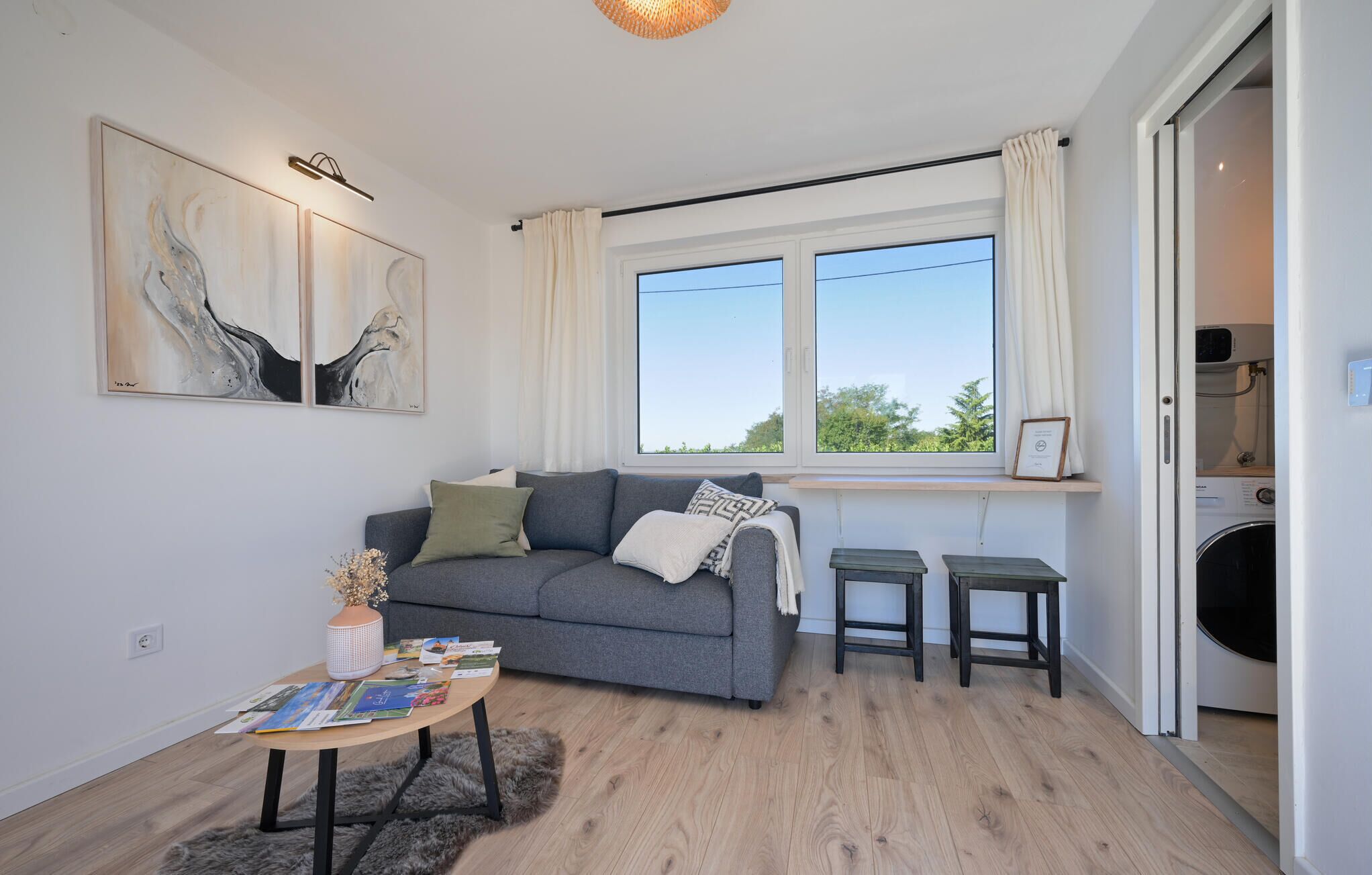 Een moderne woonkamer met een grijze bank, twee bijzettafeltjes en kunst aan de muur.
