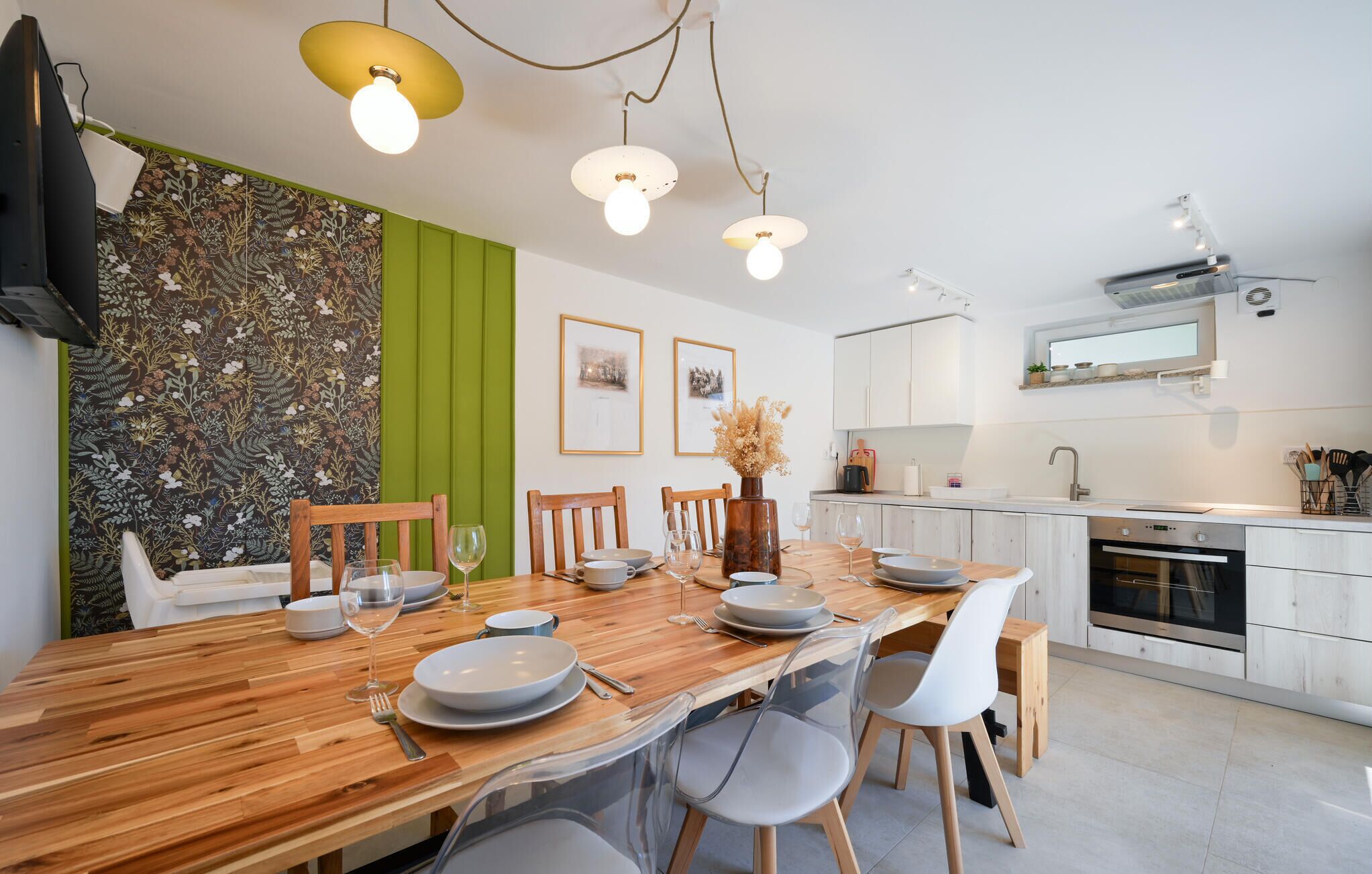 Een moderne keuken met witte kasten, een houten eettafel en een groene accentmuur.