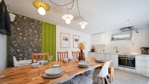 A modern kitchen with white cabinets, a wooden dining table, and a green accent wall.