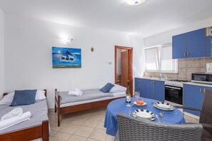 A compact hotel room with two single beds, a dining area with a table set for two, a kitchenette, and a painting on the wall. - Peaceful Retreat Apartments With Terrace (Marcana)