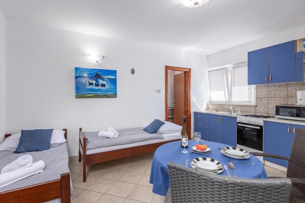 A compact hotel room with two single beds, a dining area with a table set for two, a kitchenette, and a painting on the wall. - Peaceful Retreat Apartments With Terrace (Marcana)