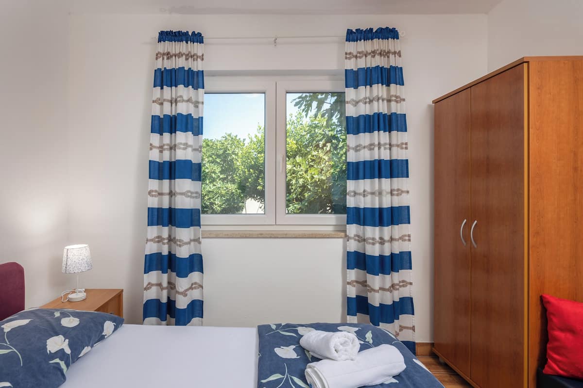 Ein Schlafzimmer mit einem Bett, einem Holzschrank, einem Nachttisch mit Lampe und Vorhängen.