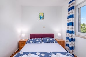A bedroom with a bed, two bedside tables, a nightstand, a wall-mounted light switch, and a window with curtains. - Peaceful Retreat Apartments With Terrace (Marcana)