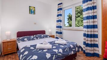 Quarto de hotel com cama, mesa de cabeceira, luminária, janela com cortinas e um quadro na parede.