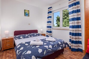 A hotel room with a bed, a nightstand, a lamp, a window with curtains, and a painting on the wall. - Peaceful Retreat Apartments With Terrace (Marcana)