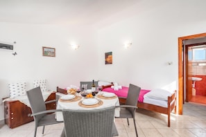 A hotel room with a dining table set for two, a bed with a pink bedspread, and a bathroom visible through an open door. - Peaceful Retreat Apartments With Terrace (Marcana)