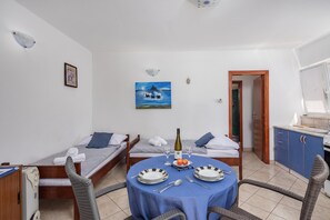 A compact hotel room with two single beds, a dining table with chairs, a small kitchen area, and a painting on the wall. - Peaceful Retreat Apartments With Terrace (Marcana)