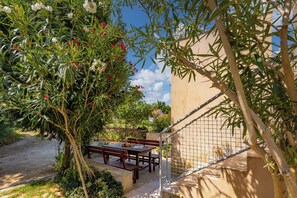 Eine Terrasse im Freien mit einem Holztisch und Bänken, umgeben von Grünpflanzen und einer Gebäudefassade.
