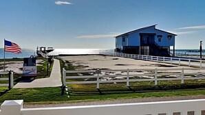 Ein Strandhaus mit weißem Zaun, einer Flagge und einem Schild.