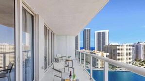 A balcony with a table, chairs, and a view of tall buildings. - Amazing 1BR Apartment + Pool + Fitness Center (Hallandale Beach)
