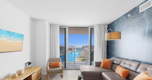 A modern living room with a sofa, a chair, a wooden console table, and a large window offering a city and water view.