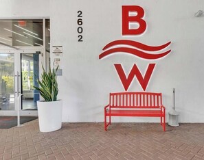 A red bench, a potted plant, and a wall with a logo and address.