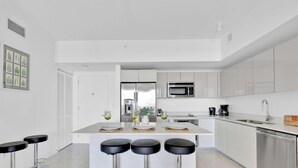 Une cuisine moderne avec des meubles blancs, un îlot central doté de tabourets, des appareils en acier inoxydable et un coin bar.