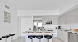 Une cuisine moderne avec des meubles blancs, un îlot central doté de tabourets, des appareils en acier inoxydable et un coin bar.