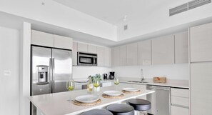 Una cucina moderna con un frigorifero in acciaio inox, un forno a microonde e una macchina del caffè. Ci sono tre sgabelli all'isola e un lavello con rubinetto.
