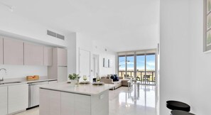 A modern kitchen with a central island, a dining area with a view, and a living space with a sofa and chairs.