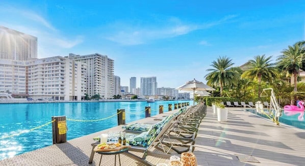 A poolside area with lounge chairs, a dining table with food, and a view of the city skyline.